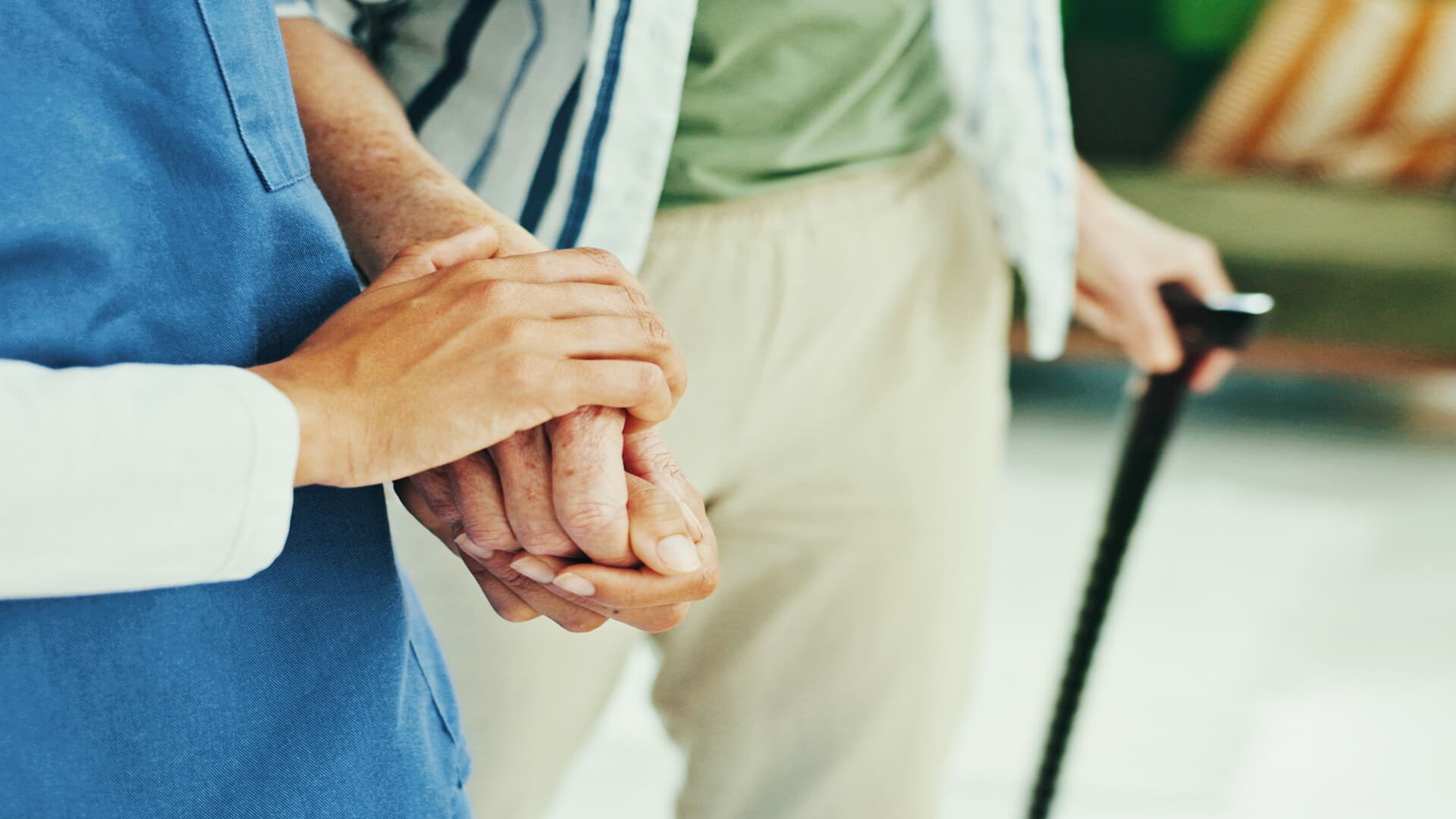 Nahaufnahme einer faltigen älteren Hand, die sanft von einer jüngeren Hand gehalten wird