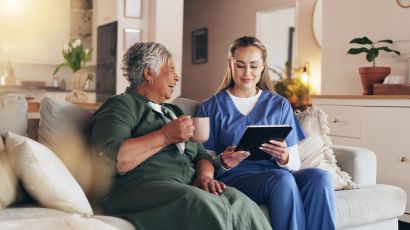 Ältere Dame sitzt lachend mit ihrer Begleitung gemeinsam auf dem Sofa