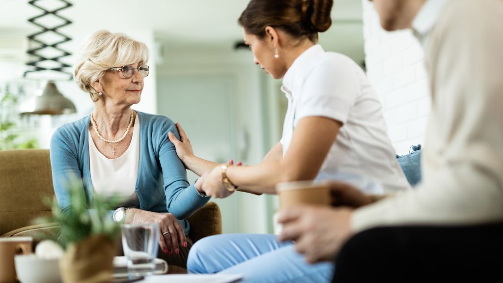Pflegekraft im Betreuungsgespräch mit einer älteren Frau im Sessel